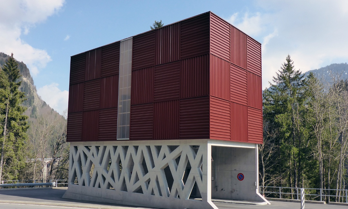 Silo modulaire architectural rouge avec support en béton filigrane, traversé par une route